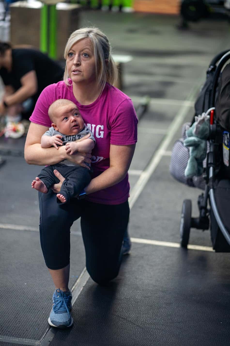A mom holding her baby while she lunges during Diapers and Dumbbells at Shark Bite Fitness