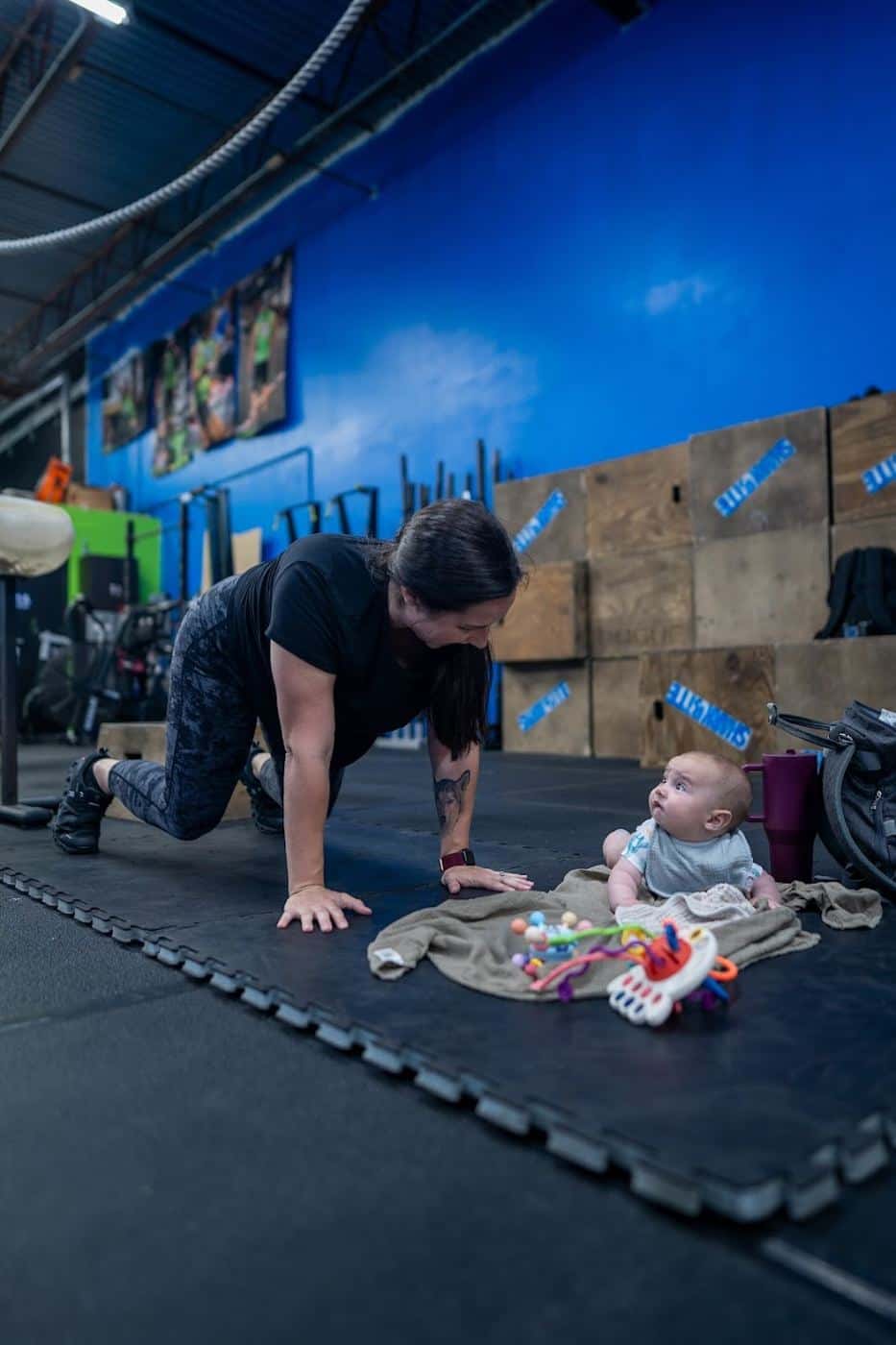 A mom planking on the gym floor next to her baby