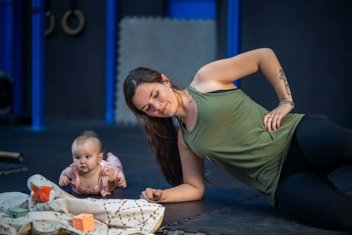 A mom in a side plank with her baby playing beside her